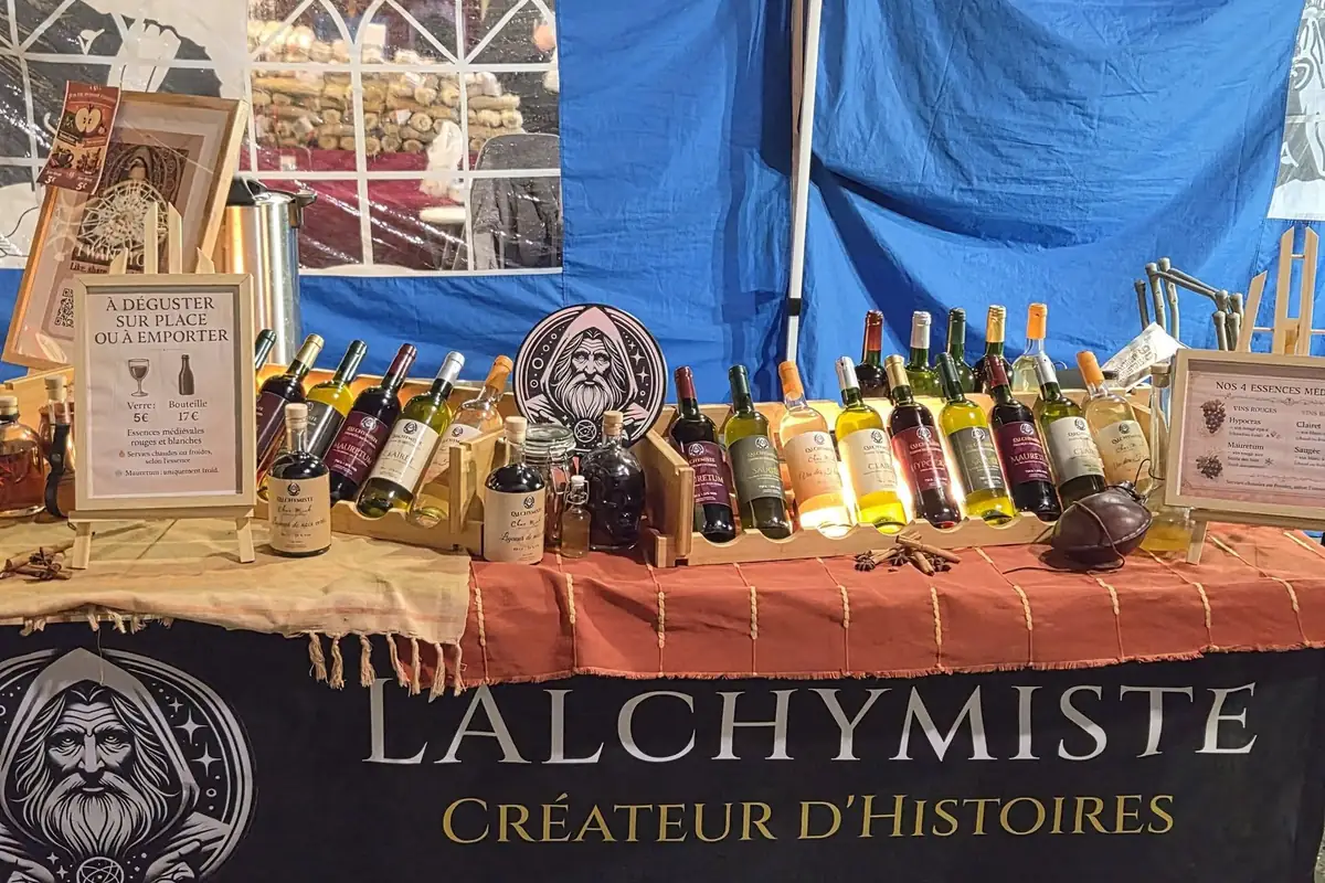 Le stand de L'Alchymiste : les bouteilles alignées sur une nappe orangée, au-dessus de la banderole « L'Alchymiste, Créateur d'Histoires »